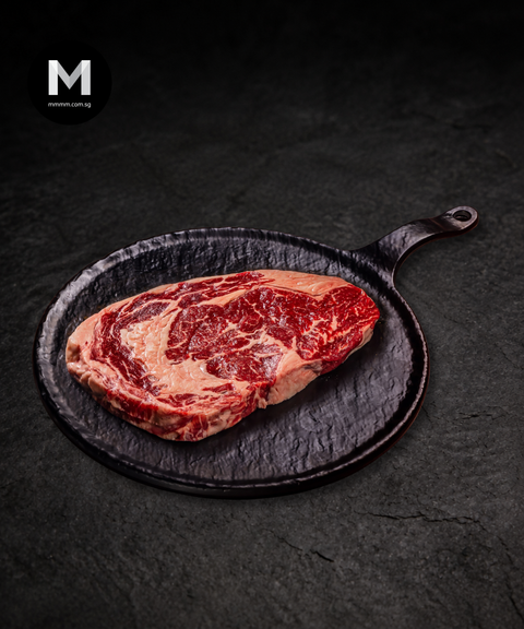 Raw grainfed ribeye on a black cast iron skillet with a dark background