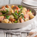 Pasta dish with Big Cheese Kransky sausages and vegetables in a white bowl on a wooden table.