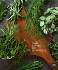 Wooden cutting board with fresh green herbs and text 'Small Leaves. Big Difference.' on a dark surface.
