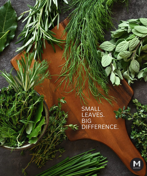 Wooden cutting board with fresh green herbs and text 'Small Leaves. Big Difference.' on a dark surface.