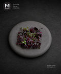 A top-down view of a small plate of purple shiso microgreens on a dark textured background, with the MMMMI logo in the top-left corner and the text 'Purple Shiso Microgreens' in the bottom-right. Perfect cress for cocktail or eating with Sashimi.
