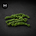 Green peppercorns on a dark textured surface with 'M' logo in corner.