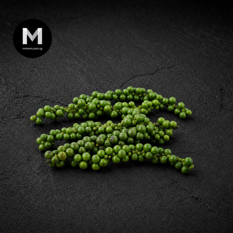 Green peppercorns on a dark textured surface with 'M' logo in corner.