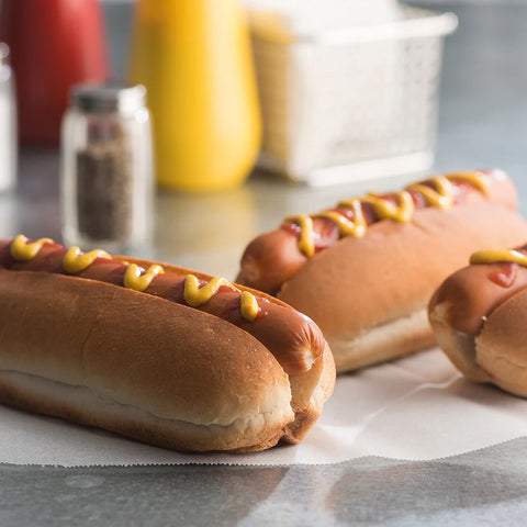 Two hot dogs with mustard on buns on a paper towel, blurred background