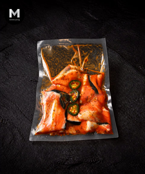 Vacuum-packed NZ King Salmon bones marinated in Cajun spice blend with jalapeño slices, on black background