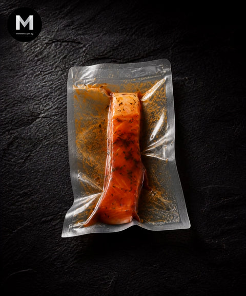 Vacuum-packed NZ King Salmon fillet marinated in Cajun spice blend, flesh side up on black background