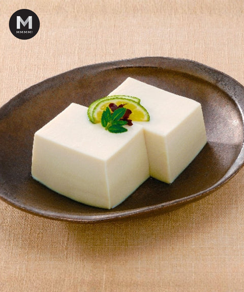 Two pieces of white tofu on a brown plate with garnishes with Sansho and Lime. The Japanese cold tofu dish.