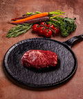 Raw wagyu beef tenderloin on a black plate with vegetables on a rustic surface