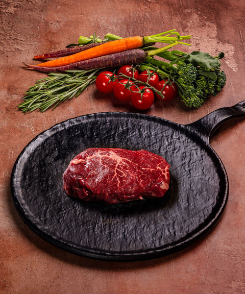 Raw wagyu beef tenderloin on a black plate with vegetables on a rustic surface